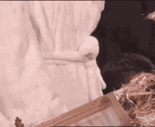 a person in a white robe is standing next to a picture frame and a pile of hay .