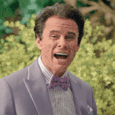 a man wearing a purple suit and purple bow tie is making a funny face