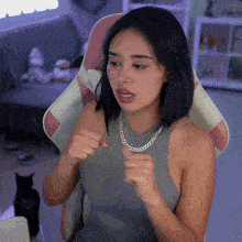 a woman wearing a gray tank top and a silver chain around her neck is sitting in a pink and white chair