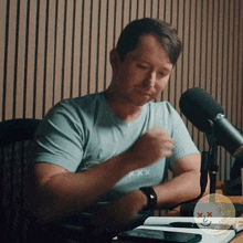 a man sitting in front of a microphone wearing a blue shirt that says xxx