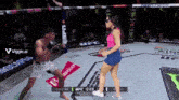 a woman in a blue skirt is standing in a boxing ring while a man in a pink shirt is boxing