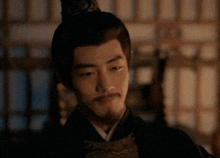 a man with a beard and a crown on his head is standing in a dark room .