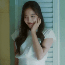 a woman in a white shirt is smiling with her hand on her chin