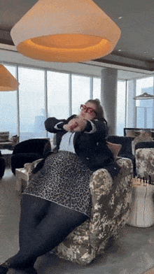 a woman in a leopard print skirt sits in a chair in front of a large window