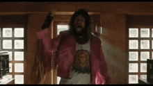 a man with long hair and a beard is wearing a pink jacket