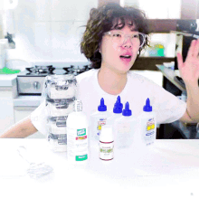 a woman is sitting at a table with bottles of glue including one that says ' acrylic ' on it