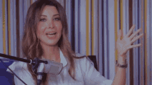 a woman sitting in front of a microphone with a striped wall behind her