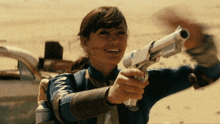 a woman is holding a gun and smiling at the camera