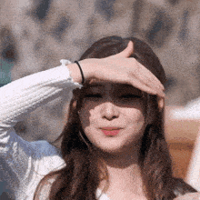 a woman covering her face with her hand while wearing a white sweater