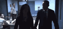 a man and a woman are holding hands in a dark room while a police officer stands in the background .