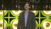 a man in a suit and blue shirt stands in front of a green wall