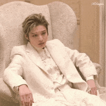 a young man in a white suit is sitting in a chair