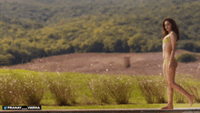 a woman in a bikini walks across a lush green field with the words pranay_varma below her