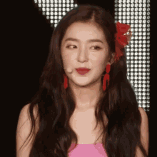 a woman wearing a pink top and red earrings with a flower in her hair