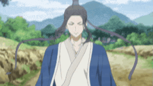 a man in a blue and white kimono is standing in a field with mountains in the background