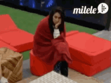 a woman is wrapped in a red blanket while sitting on a red chair .