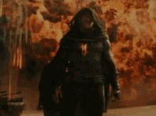 a woman in a hooded jacket is walking in front of a fire .
