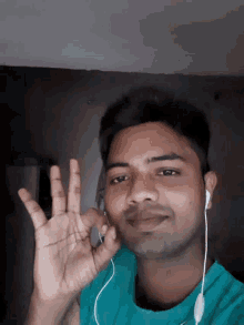 a man wearing ear buds and a green shirt holds up his hand