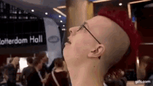 a man with a mohawk and glasses is standing in front of a sign that says ' rotterdam hall '