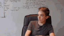 a young man sits in front of a white board with writing on it including the word mean