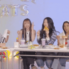 a group of people sitting at a table with balloons that say cats on the wall behind them