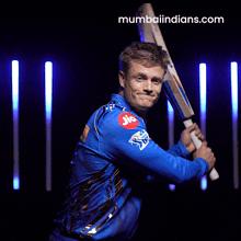 a man in a blue shirt is holding a bat and the website mumbaiindians.com is on the bottom