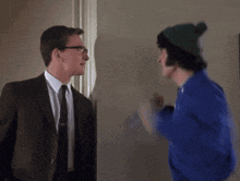 a man in a suit and tie talks to another man in a blue sweater