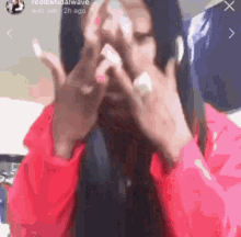a woman in a red jacket is covering her face with her hands
