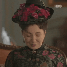 a woman wearing a hat with red flowers and a hbo logo in the corner