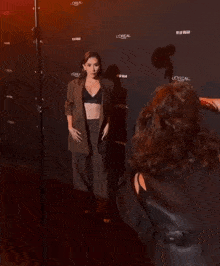 a woman in a crop top and suit stands in front of a wall that says loreal
