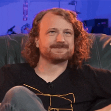 a man with curly hair and a beard is sitting on a couch and smiling