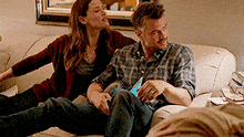 a man and woman are sitting on a couch looking at a cell phone