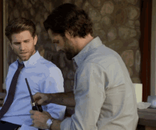 a man with a tattoo on his arm holds a walkie talkie while another man looks on