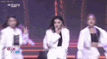 a group of women are dancing on a stage and one of them is wearing a white jacket .