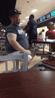 a man sits at a table in a bowling alley wearing a gray shirt that says tigers