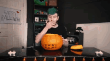 a man with green hair is eating a pumpkin in front of a happy halloween sign