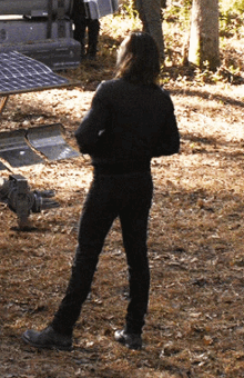 a man in a black jacket is standing in a field with a solar panel in the background