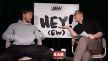 a man and a woman are sitting in front of a sign that says hey