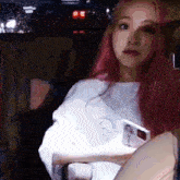 a woman with pink hair is sitting in a car with a cell phone in her hand .