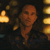 a man with a beard wearing a blue shirt with a floral pattern looks at the camera
