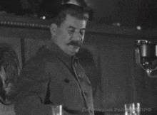 a man with a mustache is standing in front of a microphone in a room .