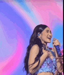 a woman singing into a microphone with a colorful background behind her