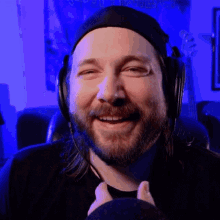 a man with a beard wearing headphones and a hat smiles