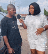 a woman is holding a microphone while talking to a man with a black shirt that says d on it
