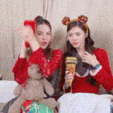 two women are sitting next to each other on a bed with a teddy bear .