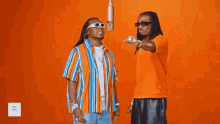 two men are standing next to each other in front of a microphone and talking to each other .