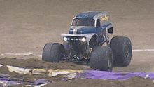 a monster truck is driving down a dirt road with a purple cloth in the background