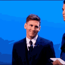 a man in a suit and tie smiles in front of a blue backdrop