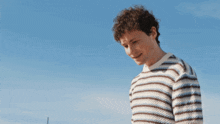 a man with curly hair wearing a striped shirt looks down