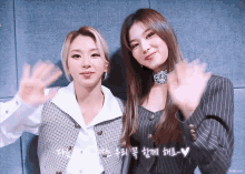 two women waving their hands in front of a wall with korean writing
